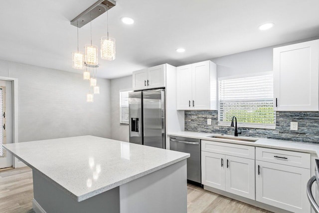 kitchen with white cabinetry, light hardwood / wood-style flooring, stainless steel appliances, sink, and a center island