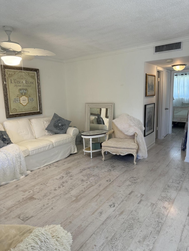 living area featuring ornamental molding, visible vents, light wood-style flooring, and a textured ceiling