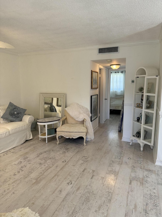 living room with ornamental molding, wood-type flooring, visible vents, and a textured ceiling