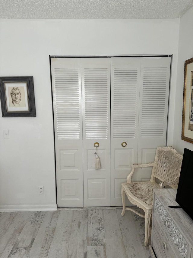 sitting room featuring baseboards, a textured ceiling, and light wood-style floors