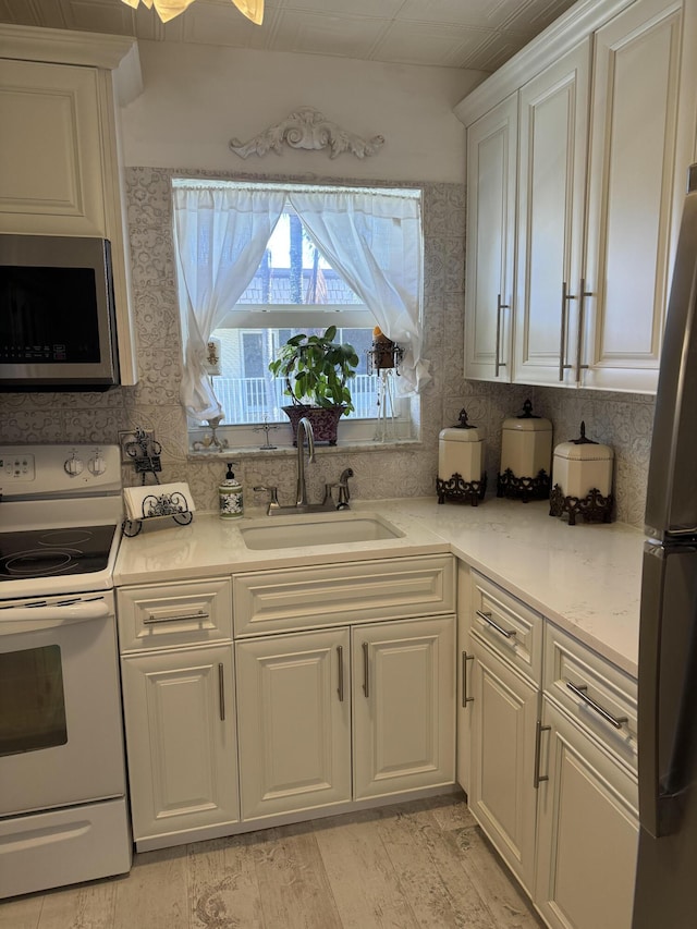 kitchen featuring stainless steel microwave, freestanding refrigerator, white electric range, white cabinetry, and a sink