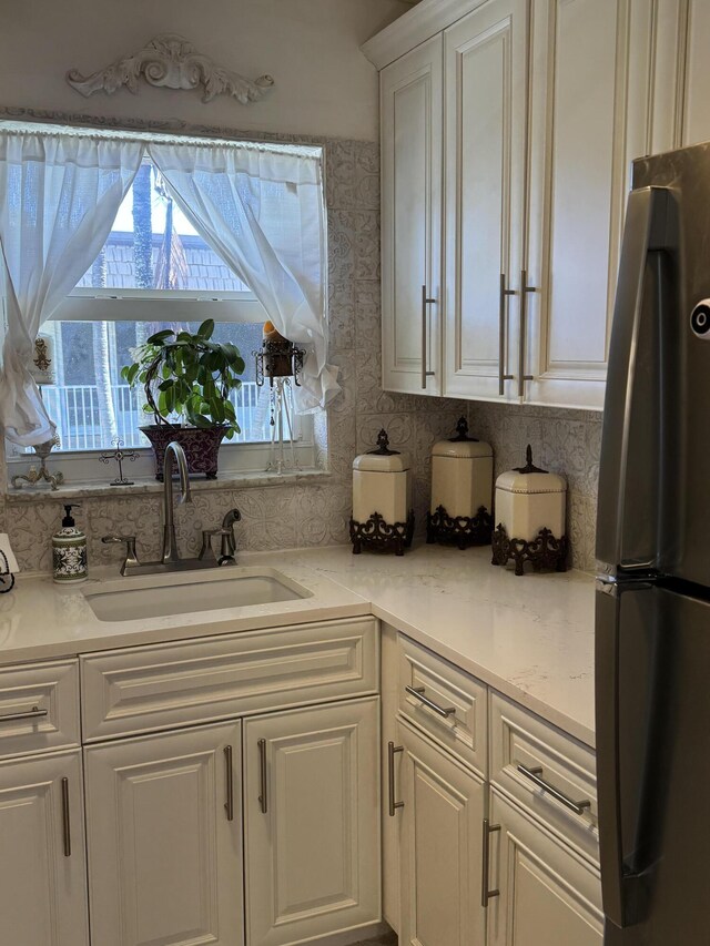 kitchen featuring white cabinetry, light stone counters, a sink, and freestanding refrigerator