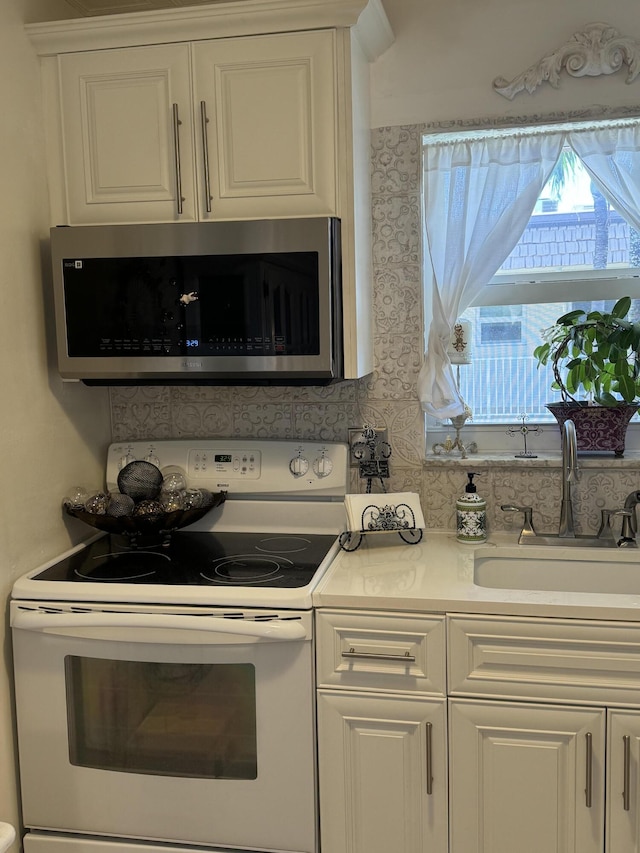 kitchen with white electric range, a sink, white cabinets, light countertops, and stainless steel microwave