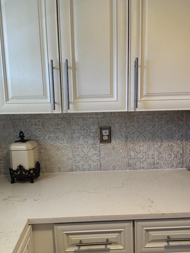 interior details featuring decorative backsplash, white cabinets, and light stone countertops