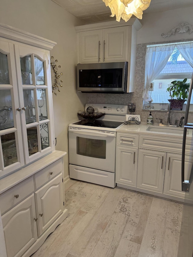 kitchen with white electric range oven, light countertops, stainless steel microwave, white cabinets, and a sink