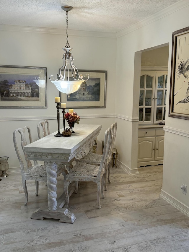 dining space with ornamental molding, light wood finished floors, and a textured ceiling