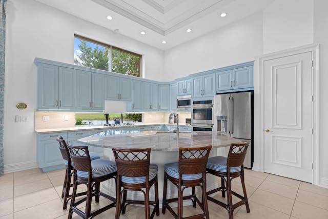 kitchen with sink, a towering ceiling, light tile patterned floors, a center island with sink, and stainless steel appliances