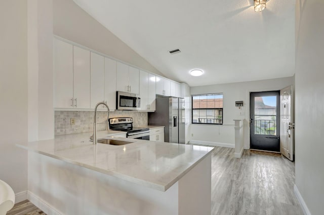 kitchen featuring kitchen peninsula, white cabinets, lofted ceiling, appliances with stainless steel finishes, and light hardwood / wood-style floors