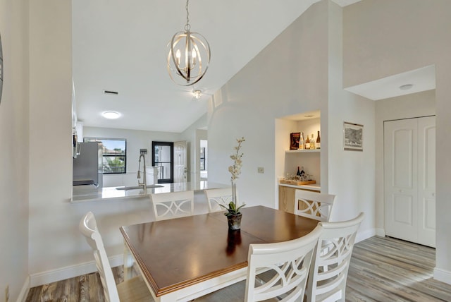 dining space with a chandelier, lofted ceiling, sink, and light wood-type flooring