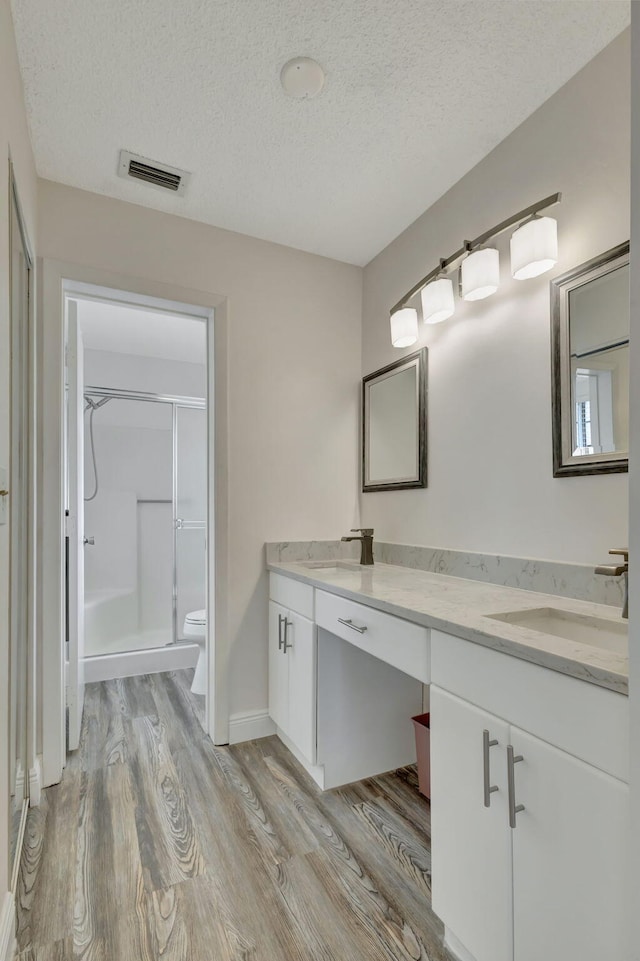 bathroom with a textured ceiling, hardwood / wood-style flooring, toilet, a shower with shower door, and vanity