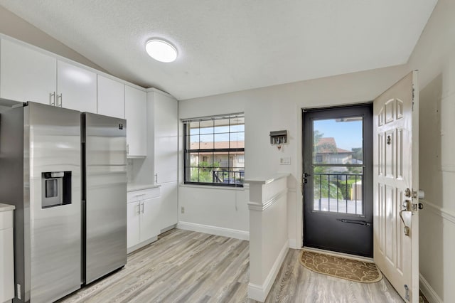 kitchen featuring light hardwood / wood-style flooring, stainless steel refrigerator with ice dispenser, vaulted ceiling, white cabinetry, and a textured ceiling