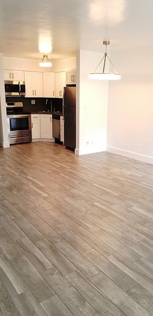 kitchen featuring stainless steel appliances, light hardwood / wood-style floors, white cabinetry, and pendant lighting