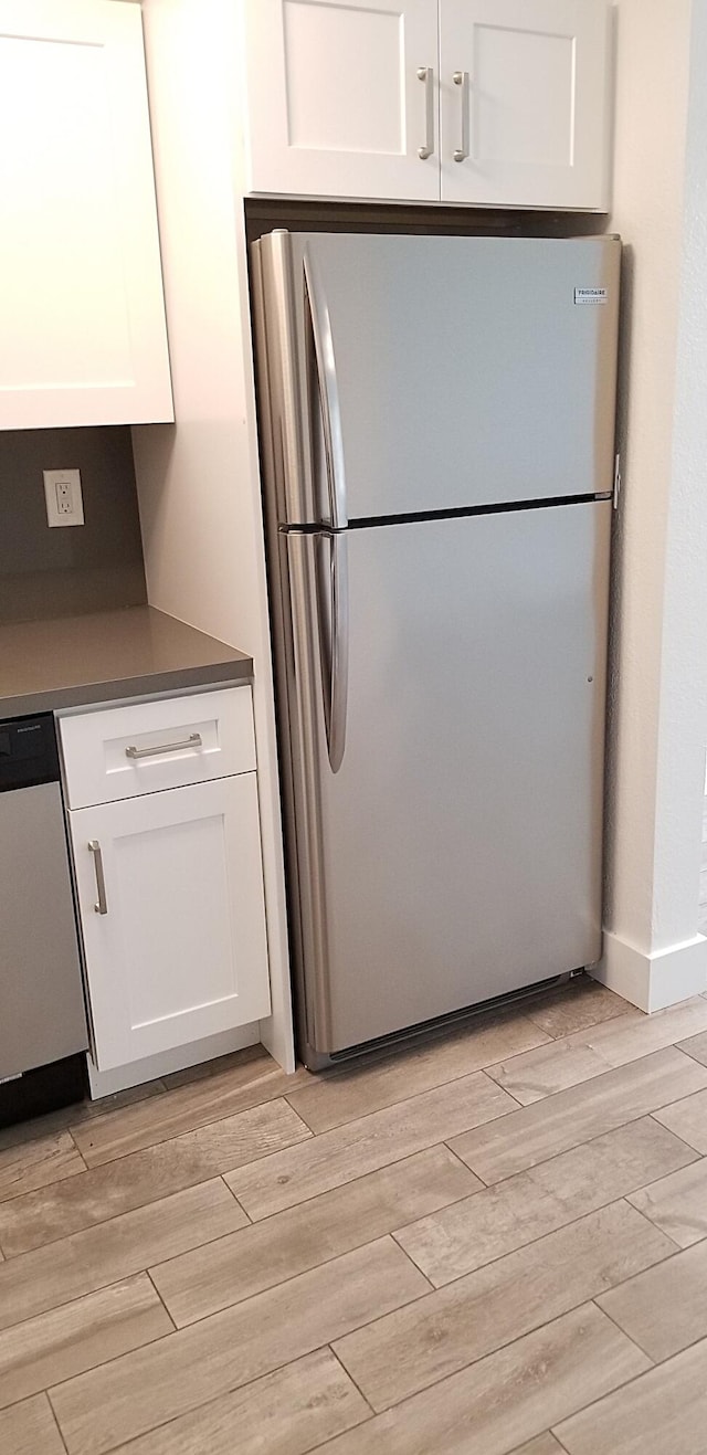 kitchen with white cabinets, light hardwood / wood-style flooring, and stainless steel refrigerator