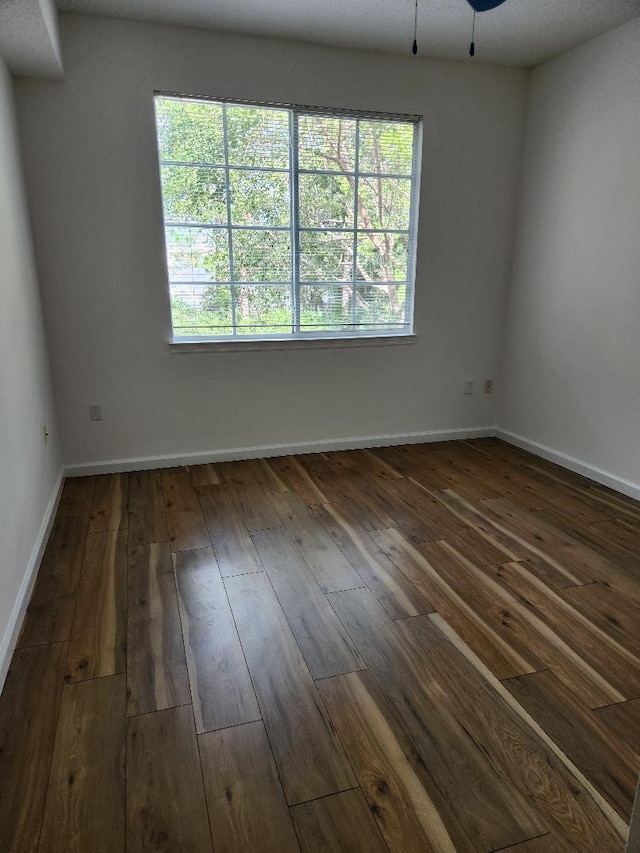 empty room featuring dark wood-type flooring, ceiling fan, and a healthy amount of sunlight