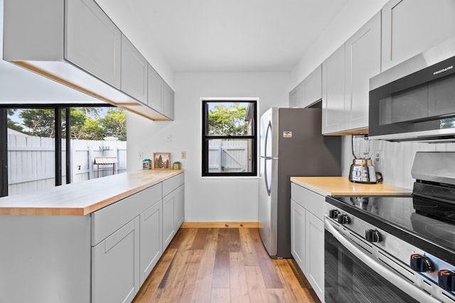 kitchen with appliances with stainless steel finishes, butcher block counters, light wood-style flooring, and baseboards