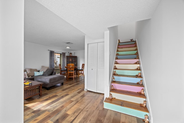 stairs featuring a textured ceiling, wood finished floors, and visible vents