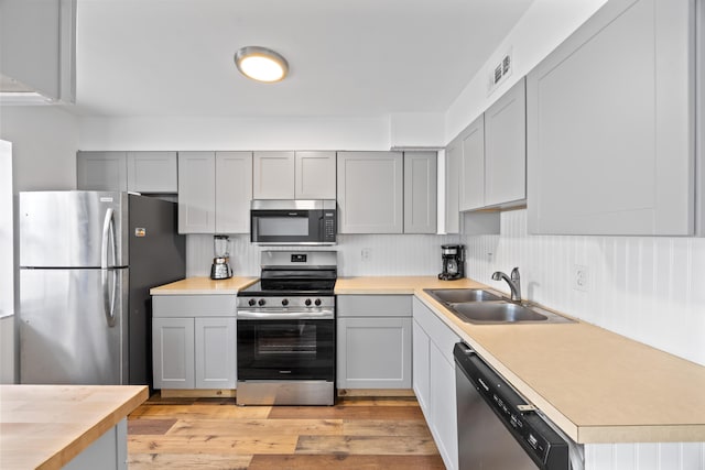 kitchen featuring gray cabinetry, a sink, visible vents, light wood-style floors, and appliances with stainless steel finishes