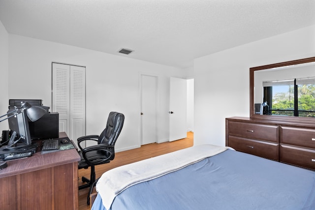 bedroom featuring a closet, a textured ceiling, visible vents, and wood finished floors