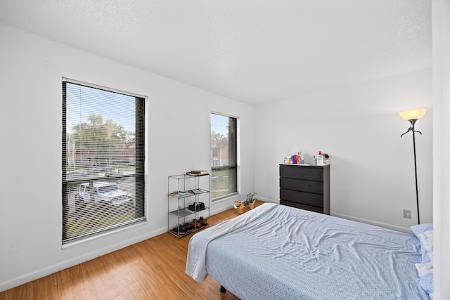 bedroom with a textured ceiling, baseboards, and wood finished floors