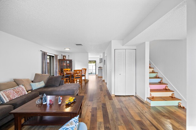 living room featuring light wood-style floors, visible vents, a textured ceiling, and baseboards