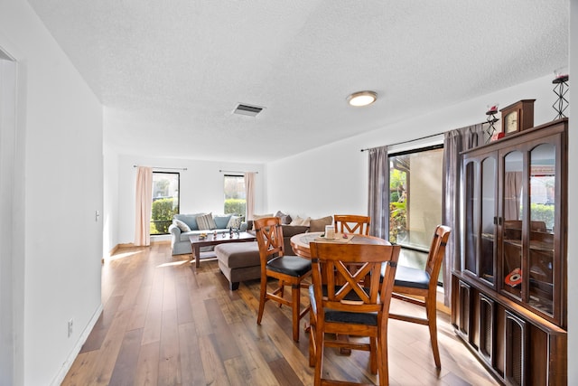 dining area featuring visible vents, a textured ceiling, baseboards, and wood finished floors