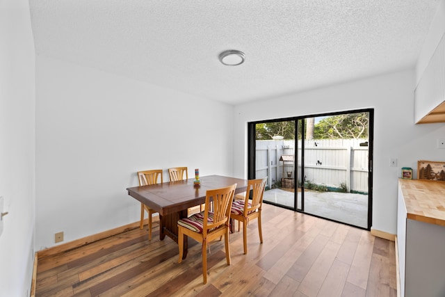 dining space featuring a textured ceiling, baseboards, and wood finished floors