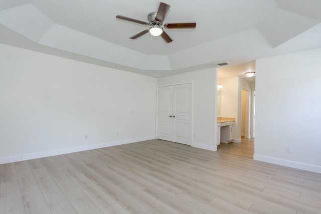 empty room with light hardwood / wood-style floors, ceiling fan, and a tray ceiling