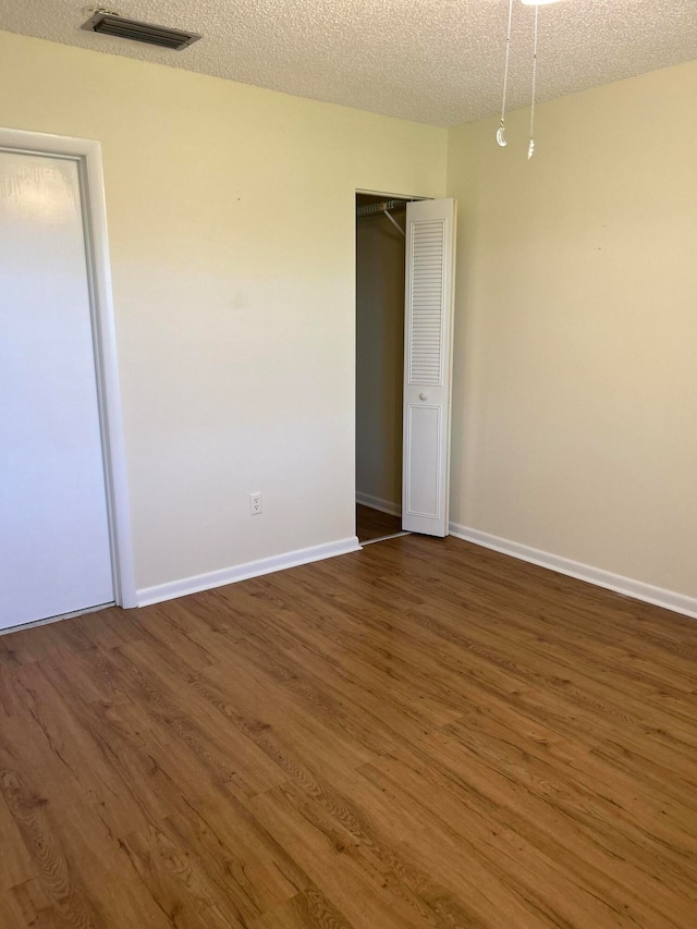 unfurnished bedroom with a textured ceiling, a closet, and dark hardwood / wood-style flooring