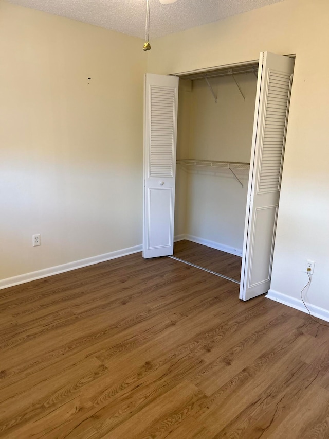 unfurnished bedroom with a textured ceiling, a closet, and dark hardwood / wood-style flooring