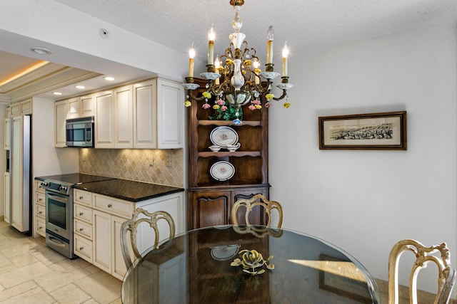 kitchen with appliances with stainless steel finishes, backsplash, a textured ceiling, a tray ceiling, and an inviting chandelier