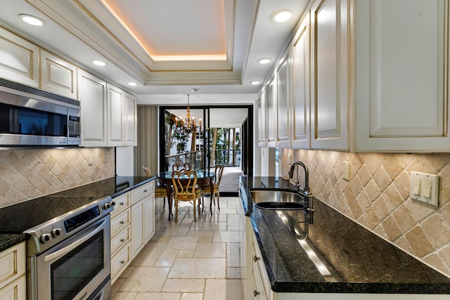 kitchen with backsplash, sink, appliances with stainless steel finishes, a tray ceiling, and a chandelier