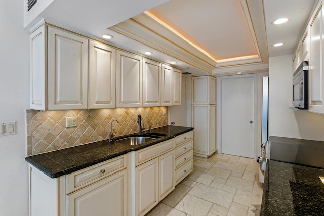 kitchen featuring sink, tasteful backsplash, dark stone counters, a tray ceiling, and range