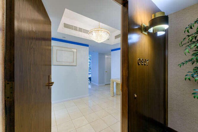 hall featuring a raised ceiling, light tile patterned floors, and an inviting chandelier