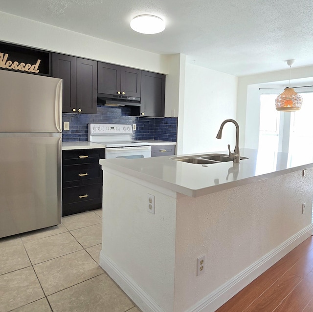 kitchen featuring sink, white electric stove, stainless steel fridge, an island with sink, and pendant lighting