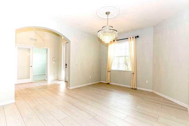 unfurnished room featuring a notable chandelier and light wood-type flooring