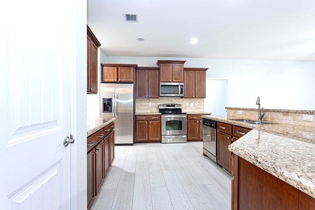 kitchen featuring light stone countertops, sink, appliances with stainless steel finishes, and light hardwood / wood-style floors