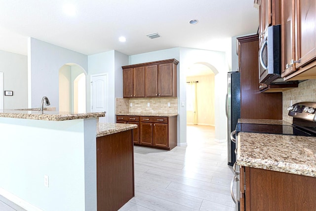 kitchen with decorative backsplash, light stone countertops, stainless steel appliances, and light wood-type flooring