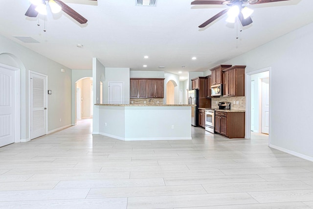 kitchen with decorative backsplash, light stone counters, stainless steel appliances, and ceiling fan