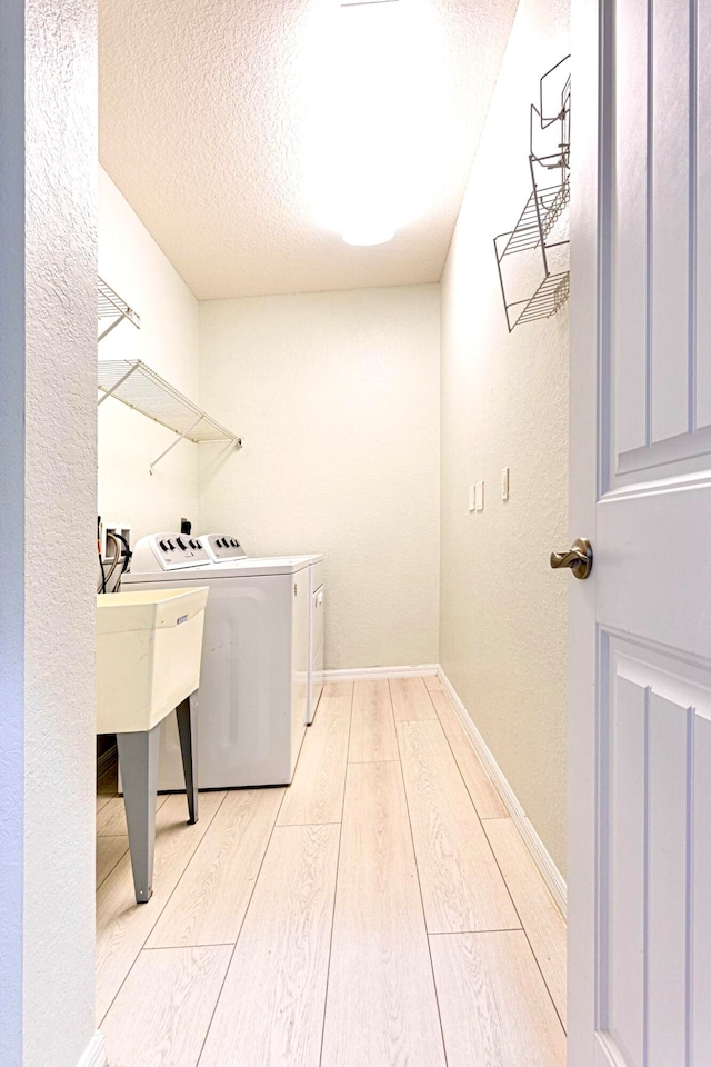 clothes washing area featuring a textured ceiling, washing machine and clothes dryer, and light wood-type flooring