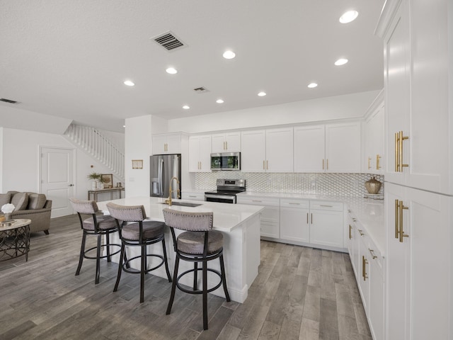 kitchen with appliances with stainless steel finishes, a kitchen bar, white cabinetry, hardwood / wood-style flooring, and a center island with sink