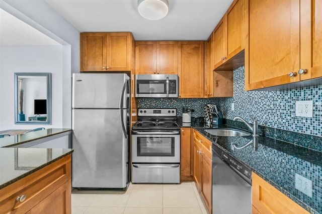 kitchen with decorative backsplash, light tile patterned floors, appliances with stainless steel finishes, dark stone countertops, and sink