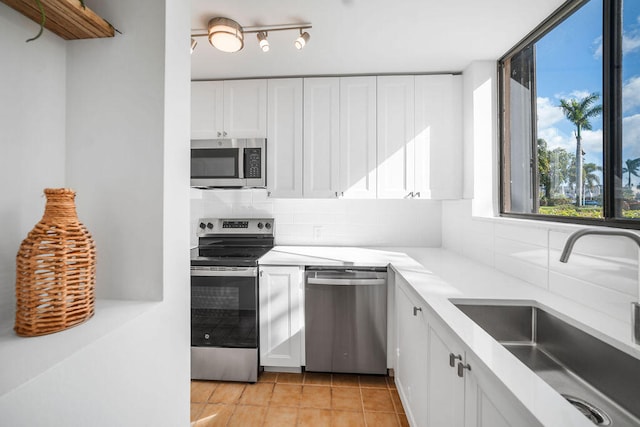 kitchen featuring sink, decorative backsplash, light tile patterned floors, white cabinetry, and stainless steel appliances