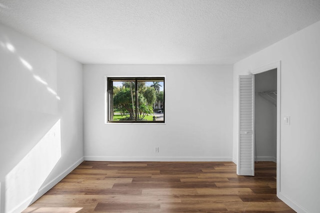 unfurnished bedroom with a walk in closet, a textured ceiling, and dark hardwood / wood-style flooring