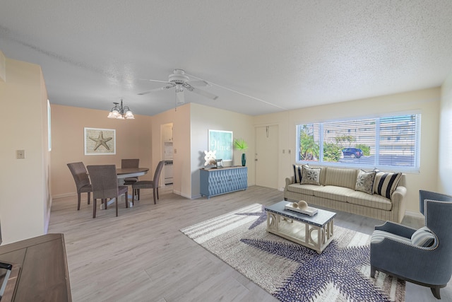 living room featuring ceiling fan with notable chandelier, light hardwood / wood-style floors, and a textured ceiling