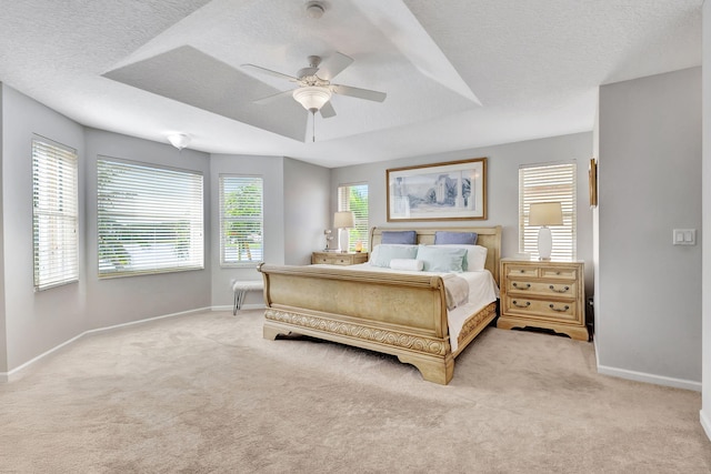 bedroom with a textured ceiling, a raised ceiling, light colored carpet, and ceiling fan