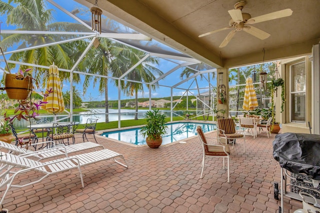 view of pool featuring a patio area, glass enclosure, ceiling fan, a water view, and a grill