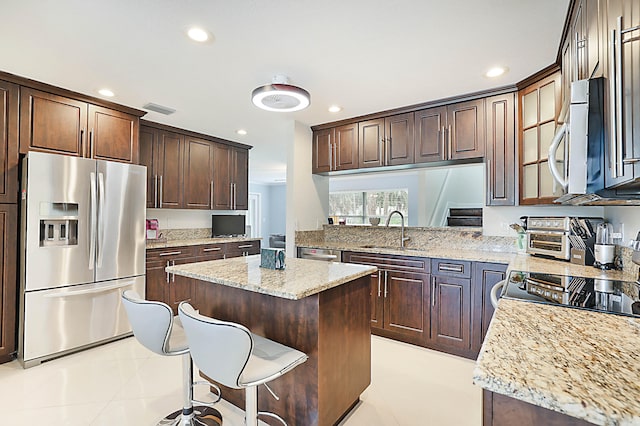 kitchen with light stone counters, appliances with stainless steel finishes, light tile patterned floors, sink, and a center island