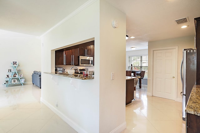 kitchen featuring light stone counters, dark brown cabinetry, light tile patterned floors, ornamental molding, and appliances with stainless steel finishes