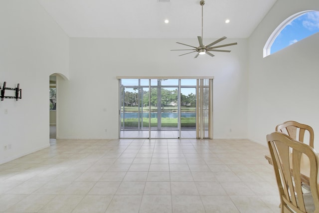 spare room with a high ceiling, a water view, a healthy amount of sunlight, and ceiling fan