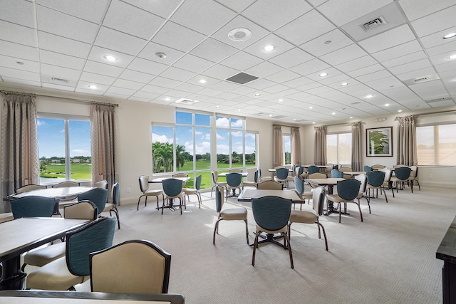 carpeted dining area with a paneled ceiling and a healthy amount of sunlight